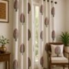 Off-white floral tree print curtain with pink flowers and grey leaves on a living room window, paired with a matching printed cushion on a wooden chair in an elegant Indian home.