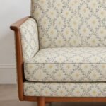 Cream floral upholstery fabric with small mustard-yellow flowers and blue-grey vines on a wooden accent chair.
