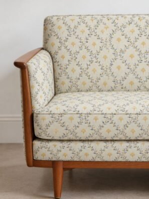 Cream floral upholstery fabric with small mustard-yellow flowers and blue-grey vines on a wooden accent chair.